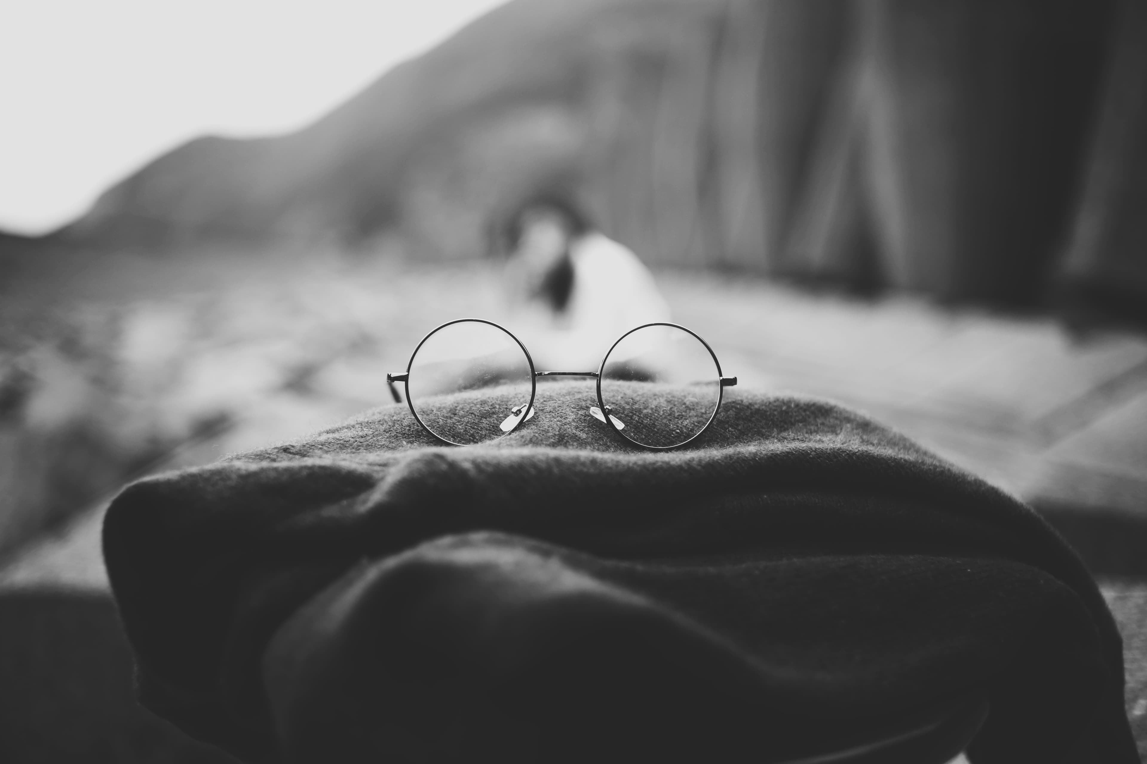 Circular glasses on a stack of folder clothes and the image is black and white.