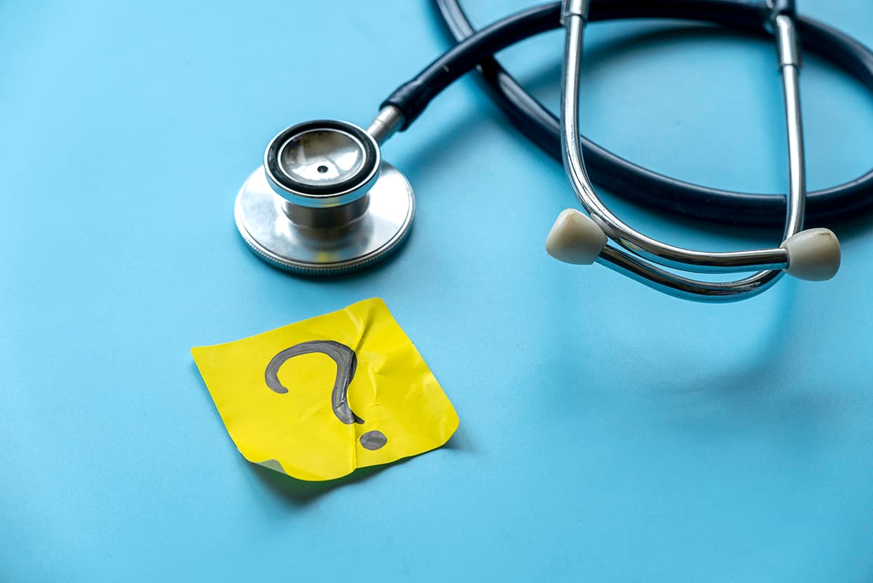 stethoscope on a blue floor or table with a. yellow post it note with a question mark