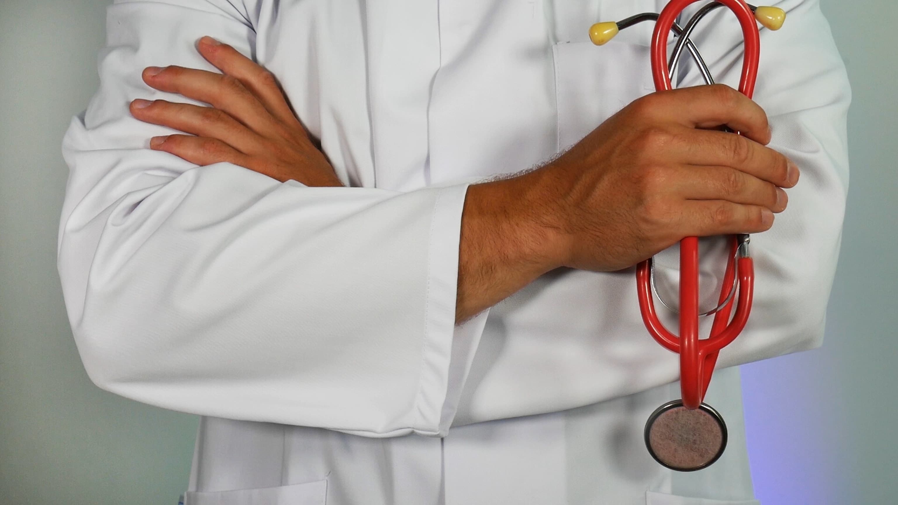 Dark skinned darker in a white lab coat hold a red stethoscope.
