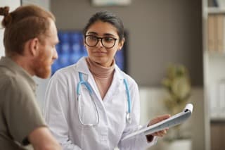 Doctor in white lab coat with blue stethoscope helping a patient
